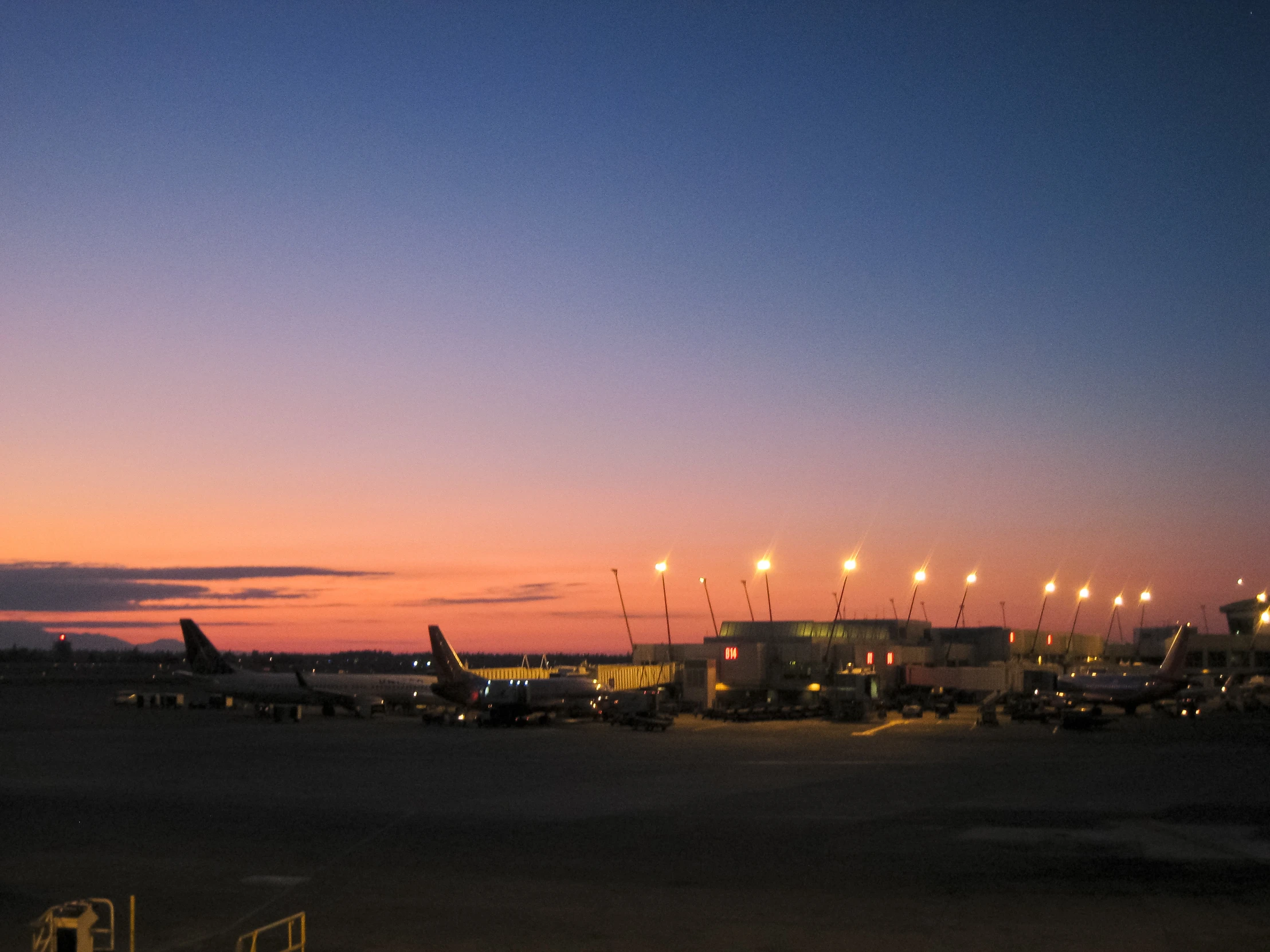 some planes are parked near a airport at dusk