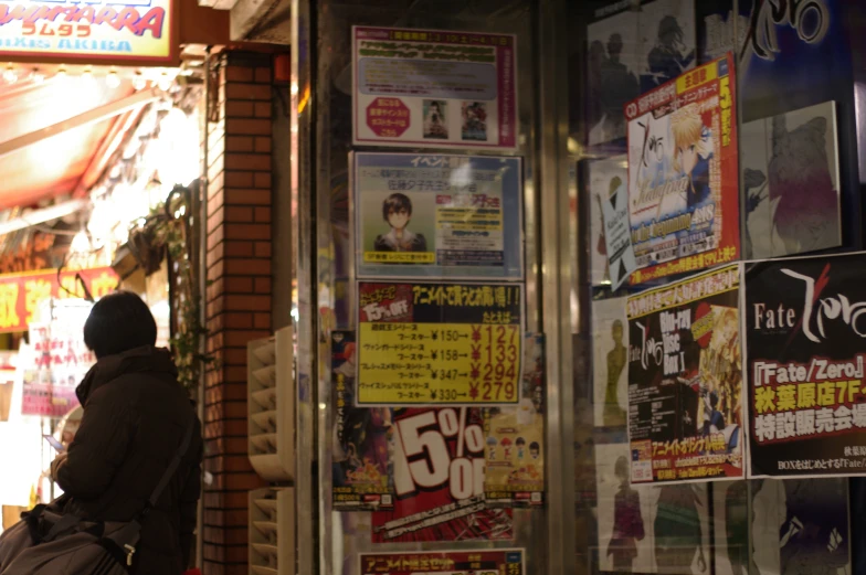 a woman stands by a building covered in posters