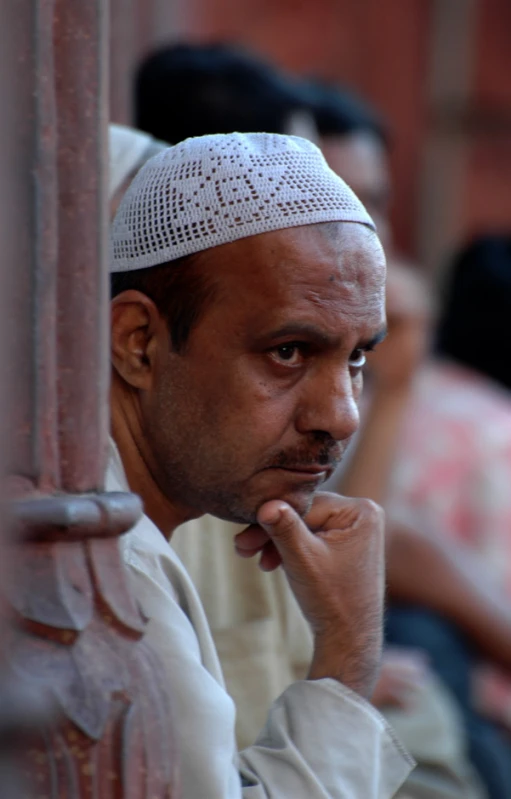 a man with an intricate hat on sitting in front of a wall