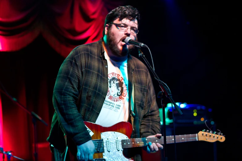 a bearded man holding an electric guitar and singing into a microphone