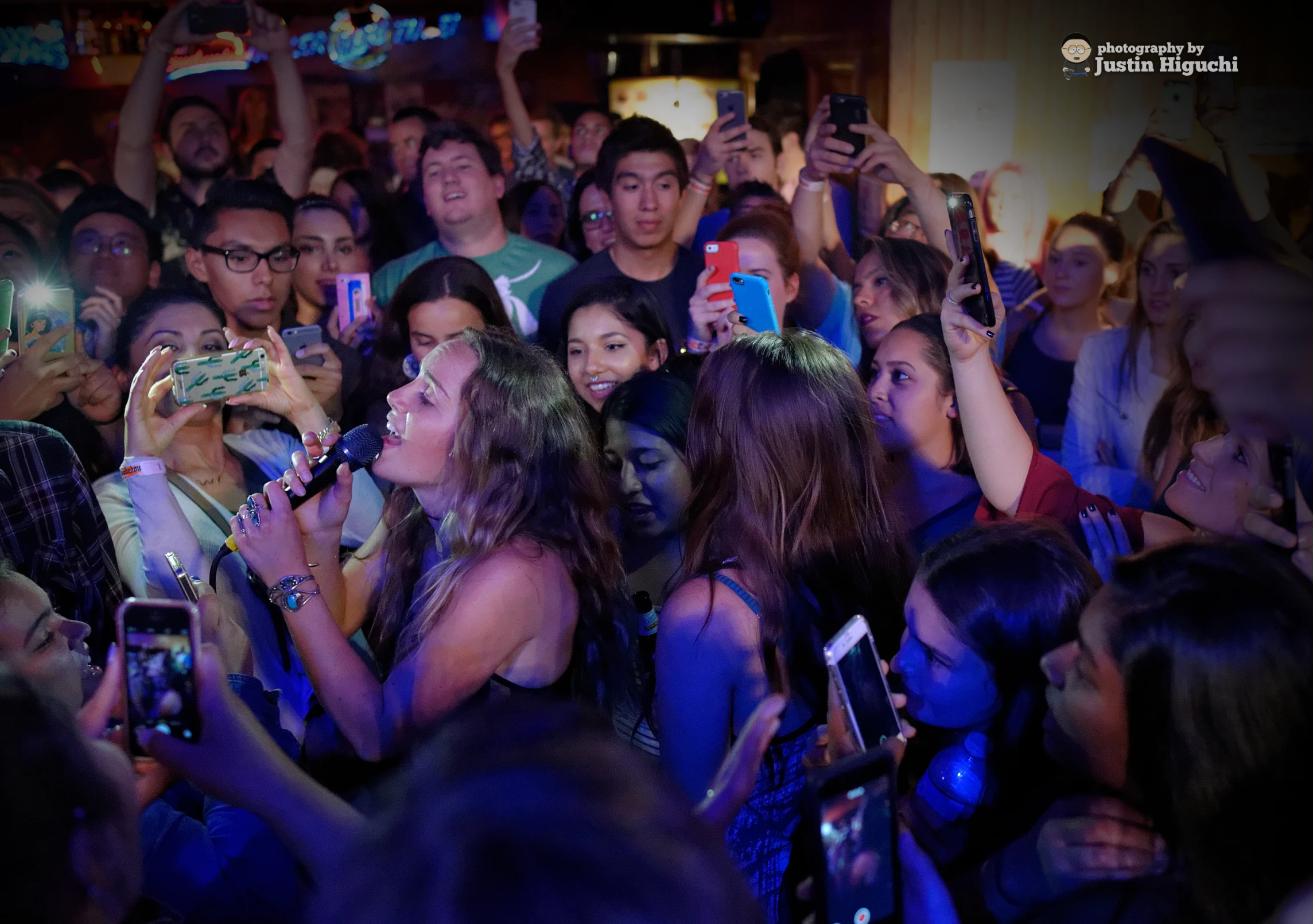 a group of people stand around taking pictures with cell phones