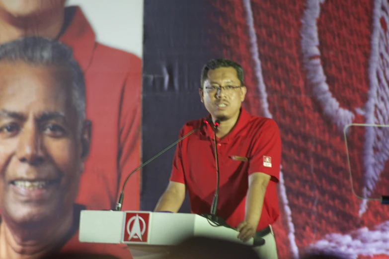 a man standing at a podium in front of a big screen