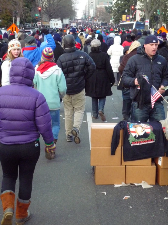 a large crowd walks on a sidewalk with lots of boxes in front of them