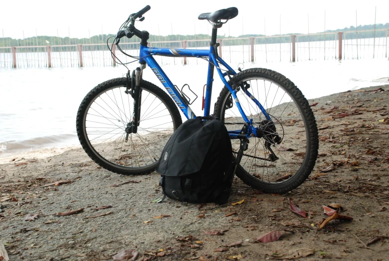 a bicycle parked next to a backpack and a body of water