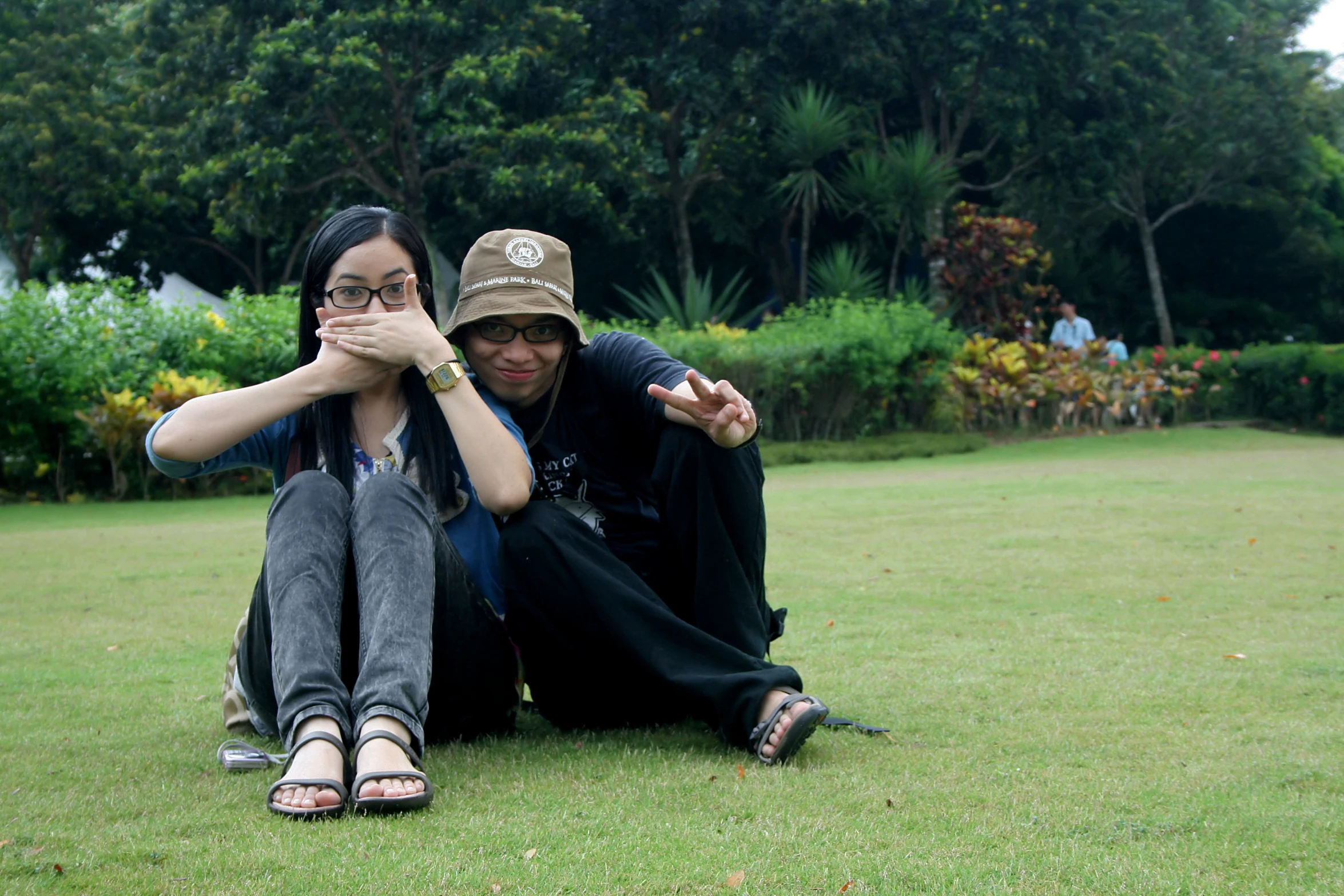 two people sit on the grass in front of trees