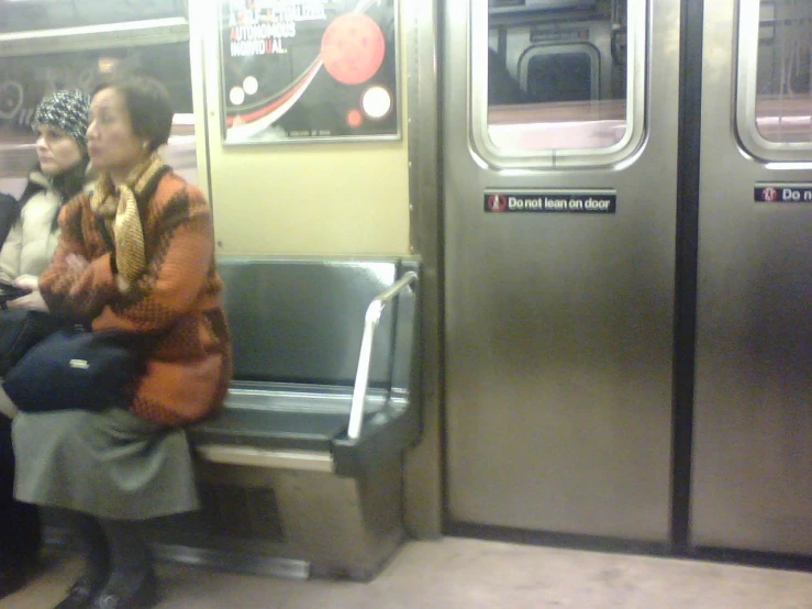 two women sitting on a subway while one holds her baby