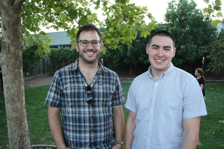 two smiling men are in a yard next to a tree