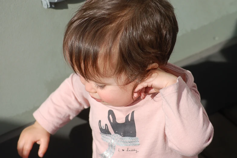 baby with pink shirt standing in sunlight looking at soing