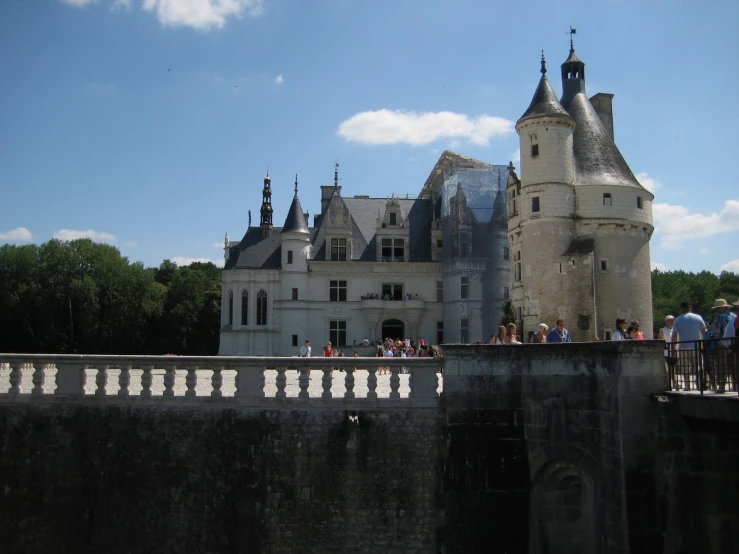 people on the bridge above a castle with people walking across the bridge