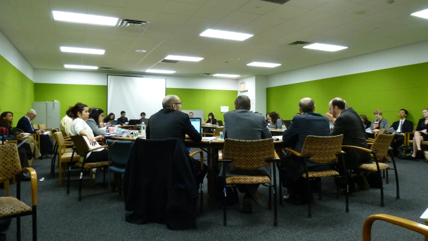 people sitting around tables looking at project on large screen