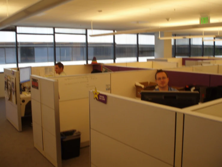 there are cubicles with people sitting and a person standing in the room