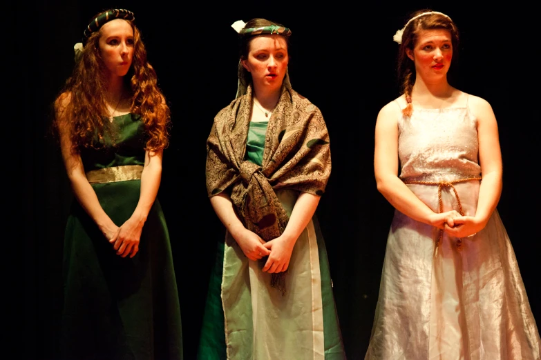 three young women dressed in long dresses are standing on stage