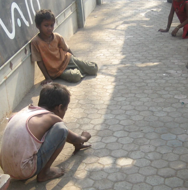 two boys sitting and playing with a cat on the sidewalk