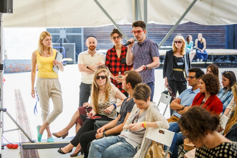 people sitting around in chairs and standing near one another