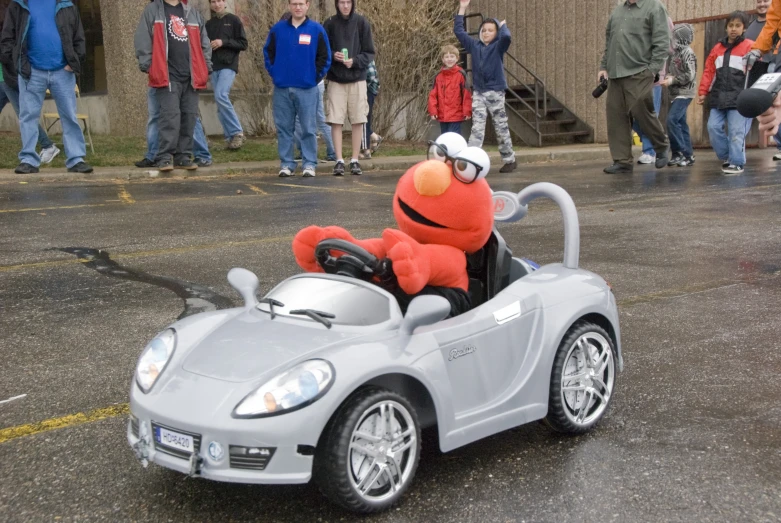 a small grey car on a wet street, with a stuffed animal in the drivers seat