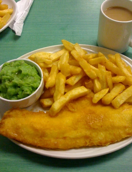 a plate filled with fish and french fries next to a side bowl full of peas