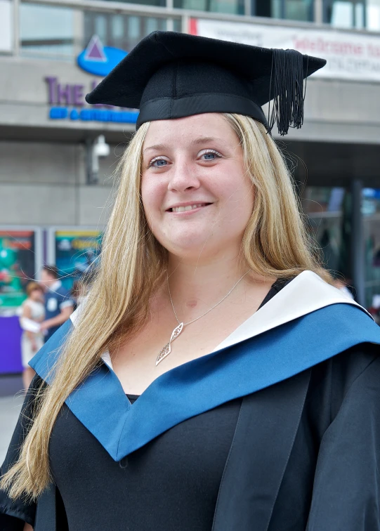 a smiling woman in graduation gown outside of the school