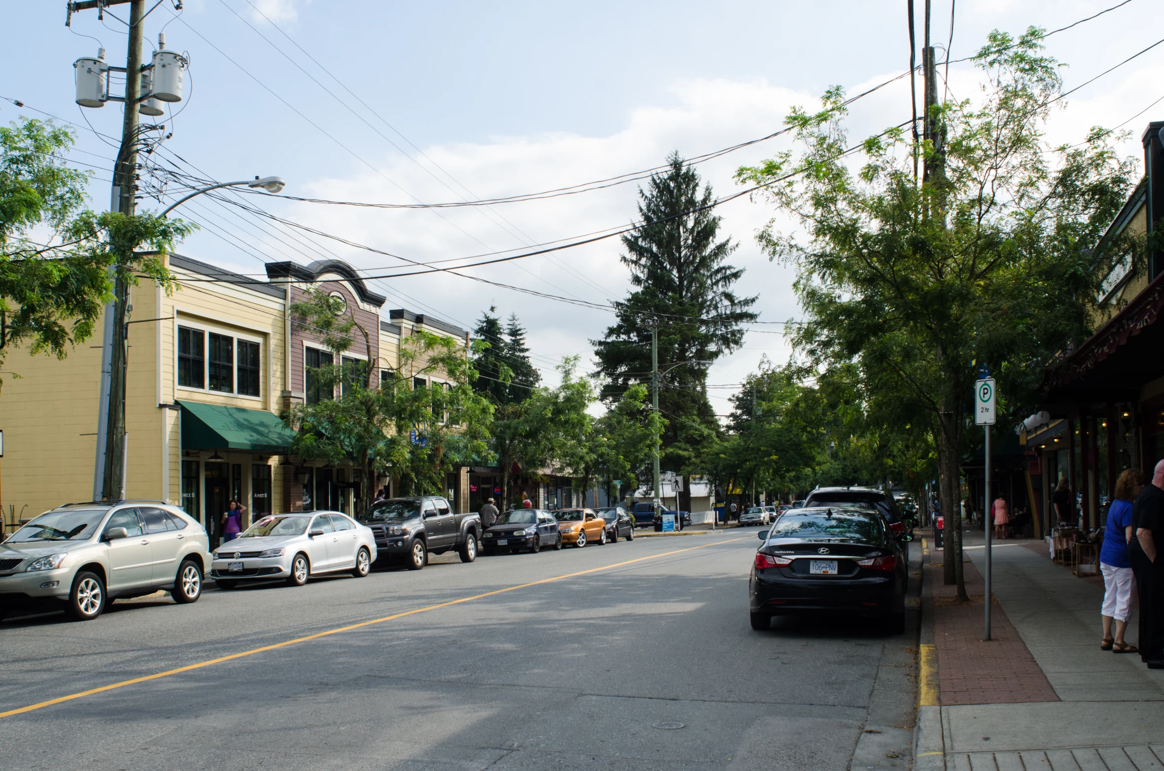 a quiet downtown street with parked cars and people waiting to ride on the sidewalks