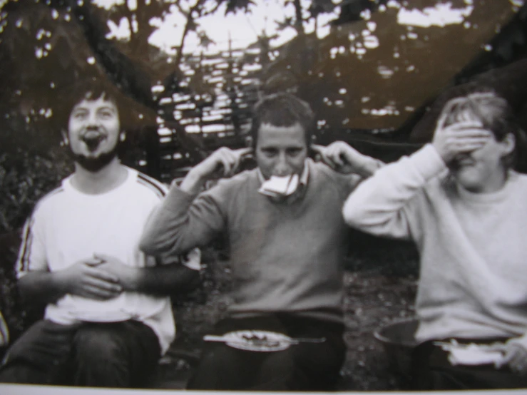 three men are eating outside while sitting on a bench