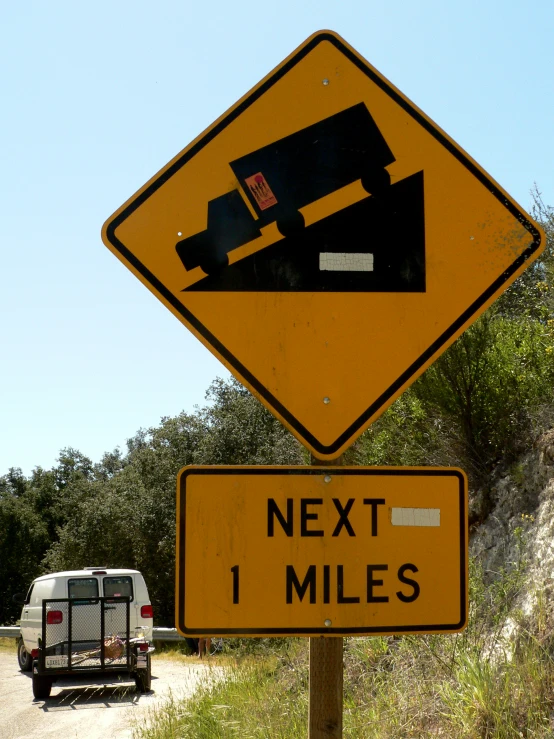 a car in a ditch next to the road that has a sign with a picture on it