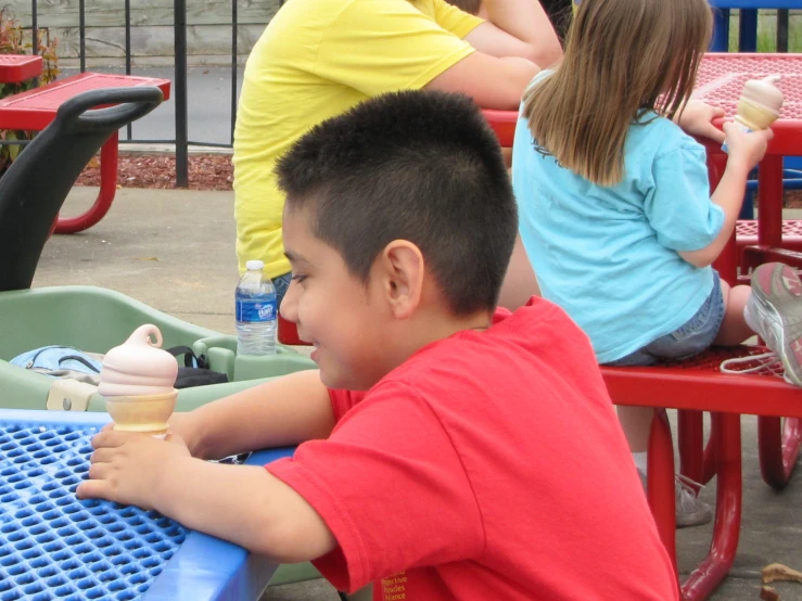 a boy eating an ice cream cone at the picnic table