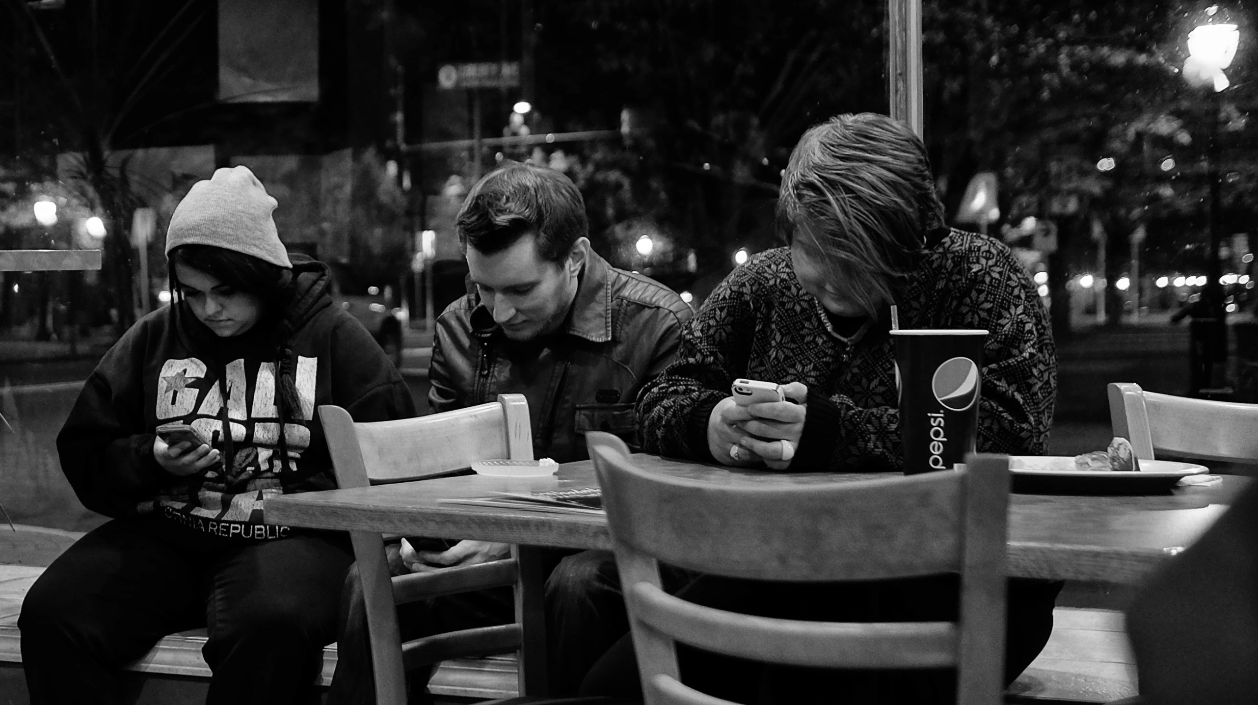 three people sitting at a table together using their cell phones