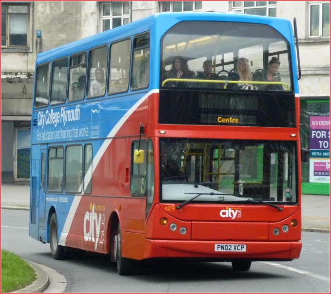 a double decker bus with passengers drives down the street