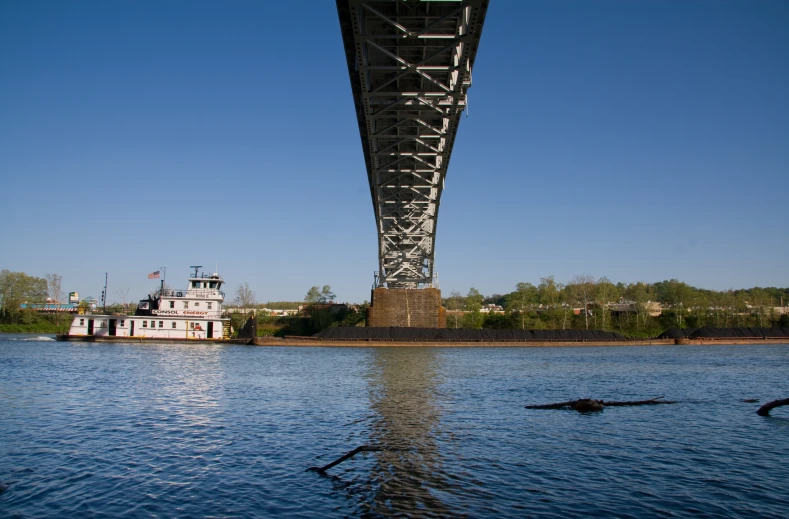 the view from the water of a bridge and a boat going under it