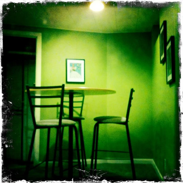 green wall with two black bar stools and one small table