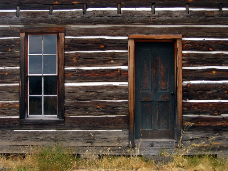 a wooden cabin with three windows, some green grass and grass