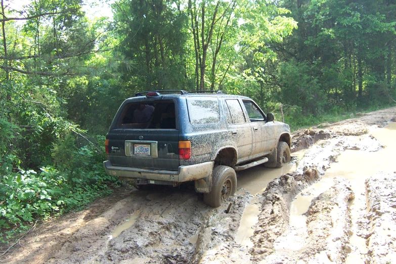 truck driving along muddy trail with trees in the back ground