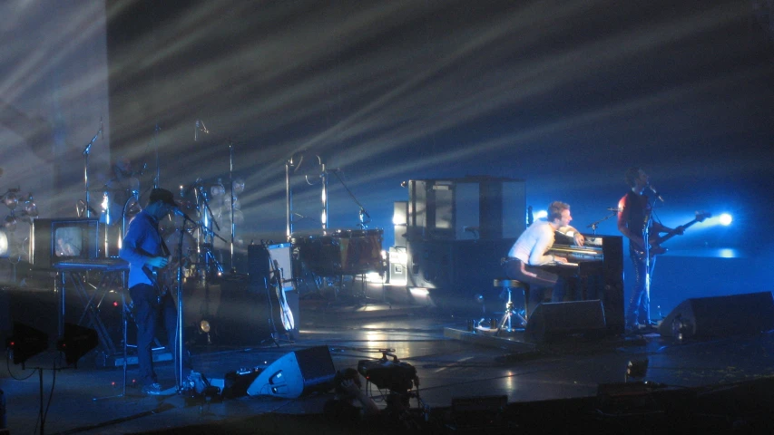 the band performs on stage with bright beams and spotlights