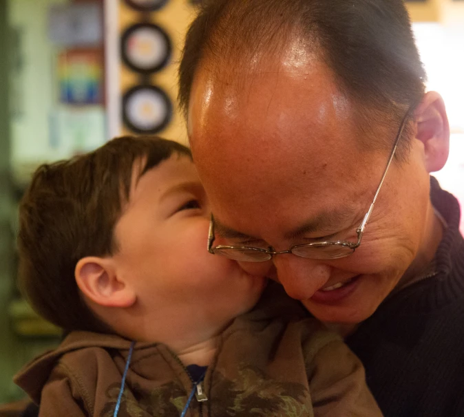 a man kisses a small boy's cheek while they both smile