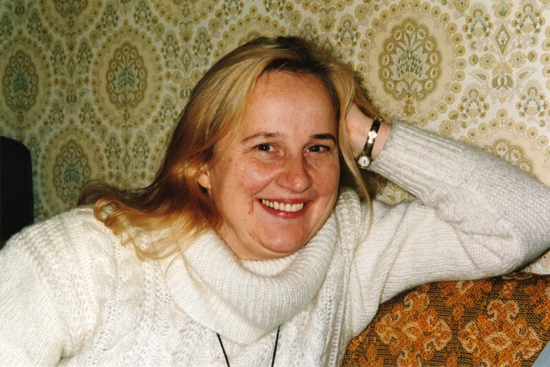 a woman smiling and sitting on a sofa in a sweater