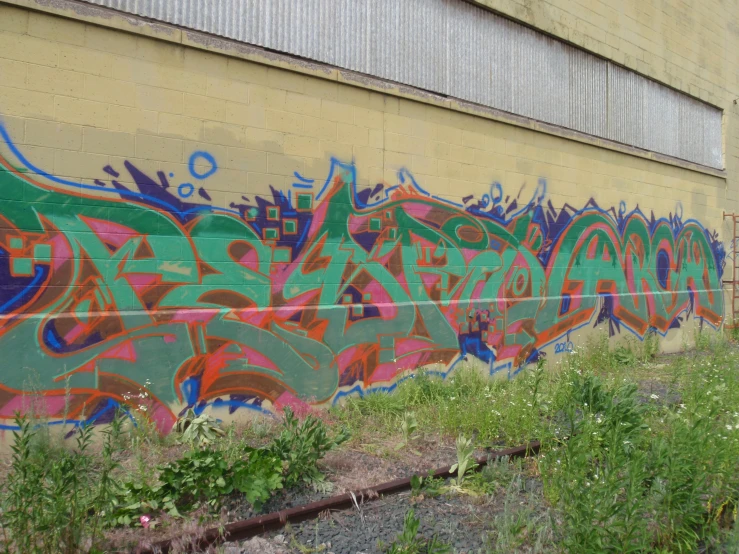 a wall with green, orange and red graffiti near train tracks