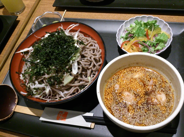 a serving tray containing an asian style bowl, plate with two small bowls full of noodles and a large bowl of veggies
