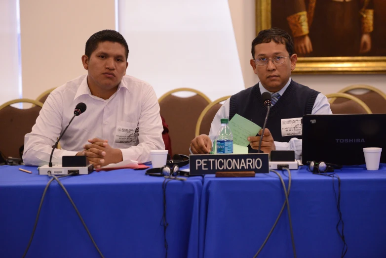 two men sit at a table with microphones in front of them