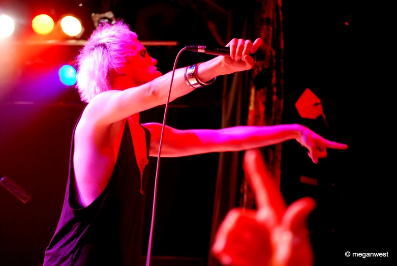 a man with pink hair and red pants singing into microphone