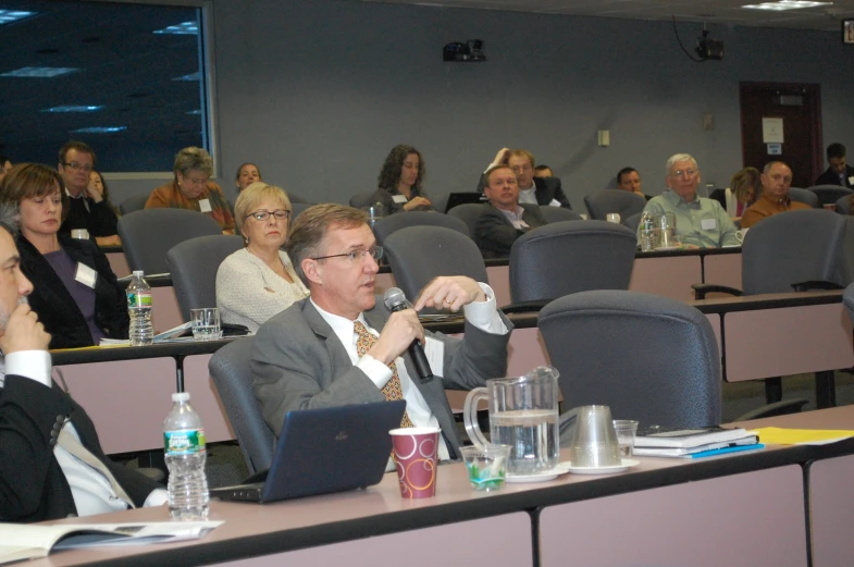 several people are sitting in a room listening to someone on his laptop