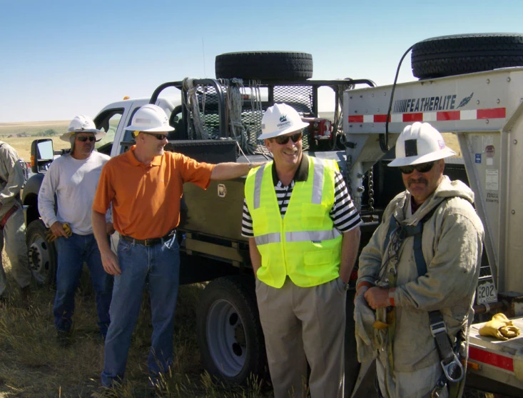 a group of men wearing safety gear and hard hats are standing in front of a tractor