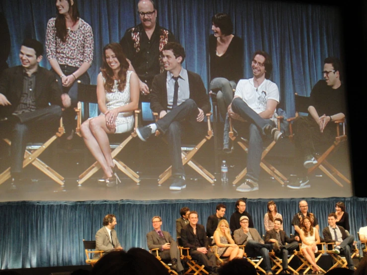 people sit on chairs in front of a stage with an image of characters