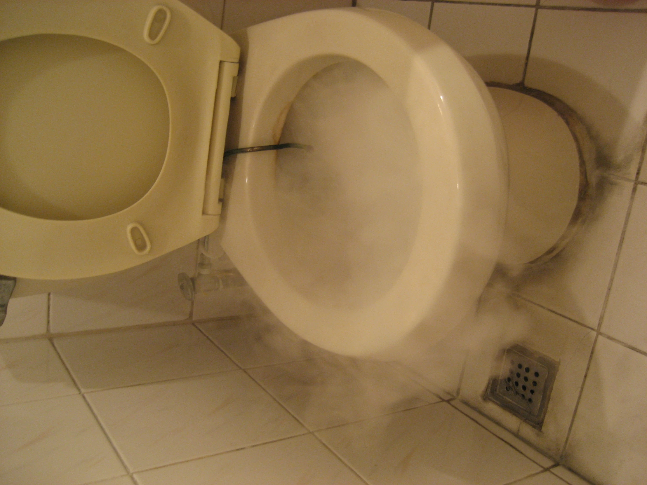 a toilet with steam rising out of it, sitting inside a tiled bathroom