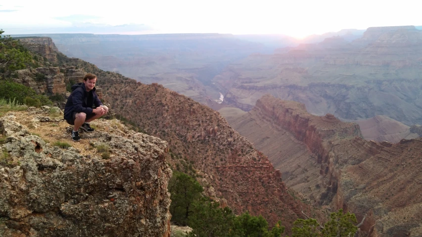 the young man sits on the edge of the cliff and admires the view