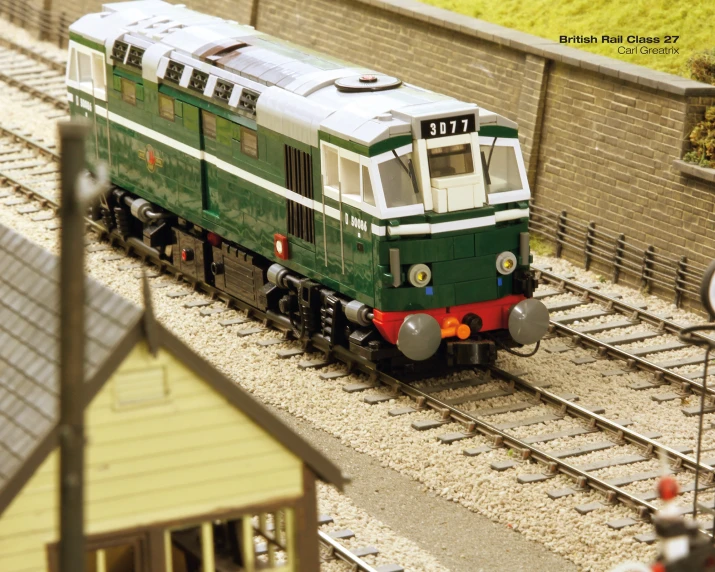 a green train sitting on the tracks next to a brick building