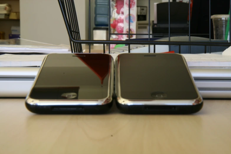 two silver cellphones sit on a wood table