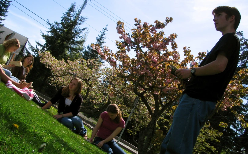 three young adults sitting on a park, one holding a wii mote