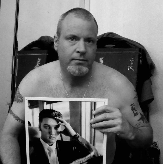 a shirtless man holds up his self portrait