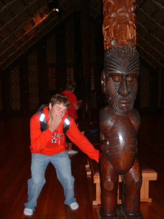 a man holding his hands up to the back of a wooden statue