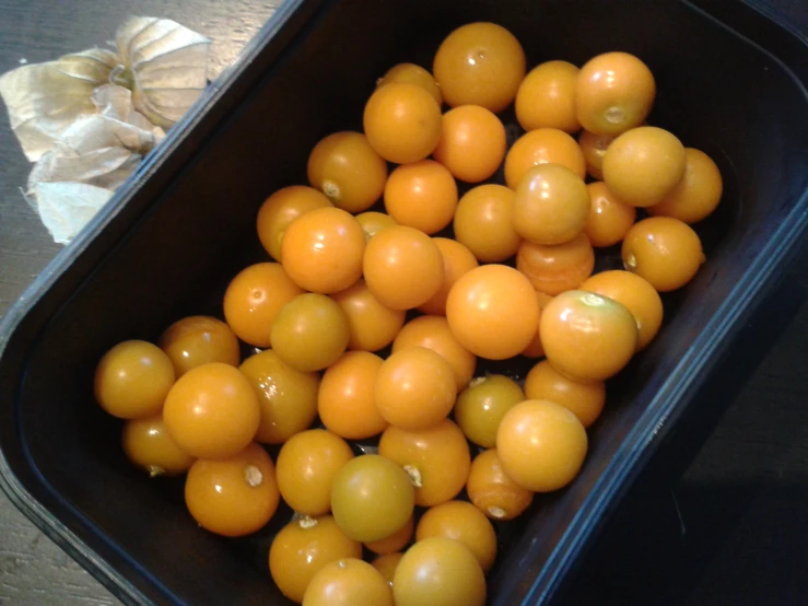 yellow tomatoes sitting in a black container on top of a table