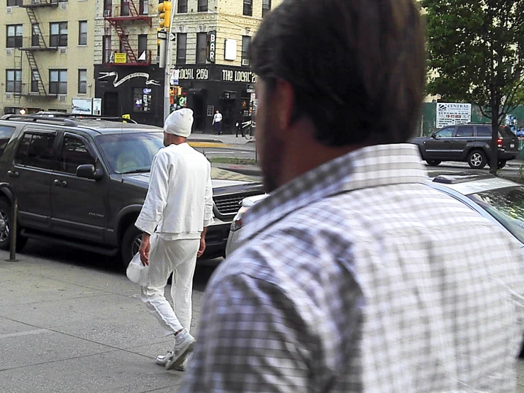 a man with white clothes and a checkered shirt crossing the street